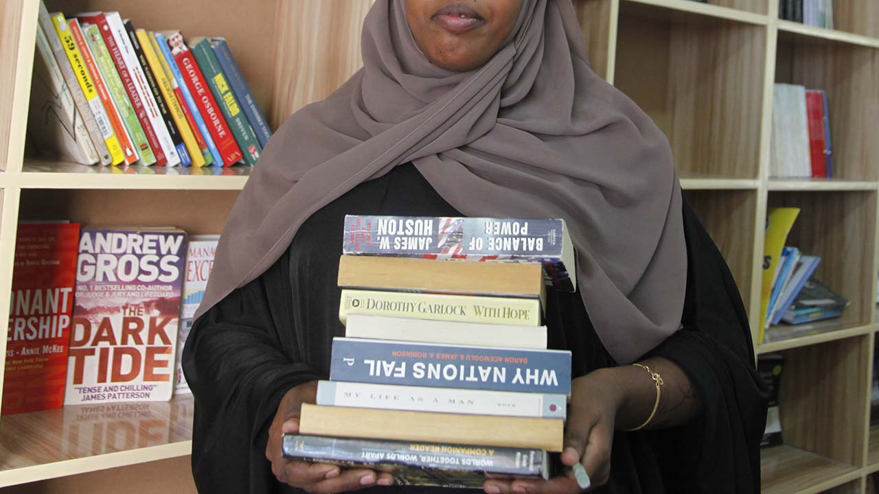 Photo of Somali woman carrying a stack of books in a library