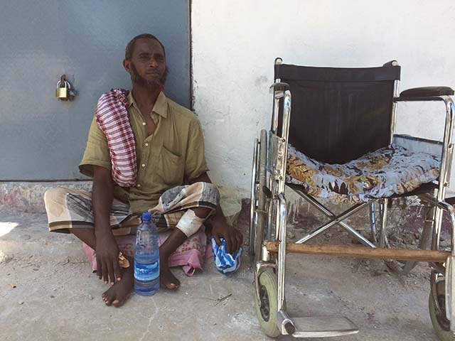 A man sits on the ground next to his wheelchair.